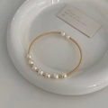 Detailopname van gouden veerarmband met natuurlijke zoetwaterparels op keramische schaal - Kleine Zoetwaterparel Armband / Goud/Wit