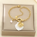 Dettaglio di un bracciale dorato con ciondoli a conchiglia, perla e pesce in una scatola - Stile Pesce (KB203142-SXSJ)