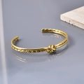 Nahaufnahme der goldenen Edelstahl-Armspange mit Knotendesign auf einem Stein - 18K Gold