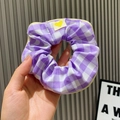 Purple and white checkered scrunchie with yellow heart label held against a wall - Large Grid / Purple