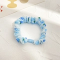 Blue polka dot scrunchie with pleated fabric design and rectangular fastener on textured background - Blue Cherry Small