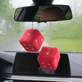 Close-up of red plush dice with silver heart patterns hanging on car rearview mirror - Red