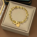 Detalle de la pulsera de cadena dorada con dije de corazón grabado en joyero beige - Hebilla OT Corazón (E152) / Dorado