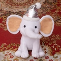 White plush elephant toy with pink ears and silver party hat on red patterned carpet - Christmas Silver Hat/White Elephant