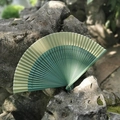 Classic Chinese green gradient folding fan with hollow carved bamboo ribs on natural mossy rock - Green