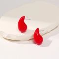 Detailed view of glossy red teardrop earrings on a white textured stone surface - Red