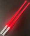 Close-up of dual glowing red LED chopsticks with white handles against dark background - Red