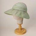 Detailed shot of pleated light green sun hat with elegant metal button on a display head - M (56-58cm) / Green