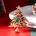 Broche sapin de Noël dorée avec strass multicolores et nœud émaillé sur un fond rouge vif - Champagne