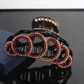 Black hair claw clip with interlocking red and gold rhinestones on reflective surface - Red Gold Rhinestones