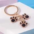 Dettaglio di portachiavi a forma di zampa di gatto dorata con smalto nero su sfondo blu - Nero