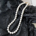 Elegant pearl necklace with white round pearls and a gold clasp on a black silk backdrop - 12mm