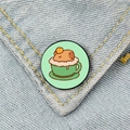 Cute capybara enamel pin in a green tea cup shown on a blue denim pocket detail - Capybara in Tea Cup