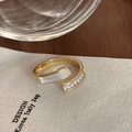 Detailaufnahme eines goldenen offenen Rings mit weißer Einlage und Steinen auf Stoff - Einstellbar Offen / Muschel-Zirkon-Stil
