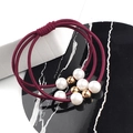 Détail d'élastiques à cheveux bordeaux avec perles blanches et billes dorées sur marbre - Bordeaux
