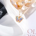 Detailed close-up of a gold butterfly necklace with gradient crystals on white silk fabric - Pink Purple