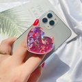 Pink heart-shaped laser glitter phone socket grip held against a silver smartphone - Expanding Stand / Pink Holographic Heart