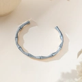Detailed macro view of an elegant silver bamboo-style knot bangle on a beige background - Open Bamboo Style (XKB0227)
