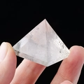 Natural white crystal pyramid with internal textures held between two fingers - 3cm