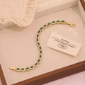 Dettaglio di pietre verde smeraldo e pavé di zirconi su un bracciale a catena dorata - Oro