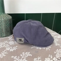 Detail of a purple-grey cotton beret cap with side label on white lace surface - Blue Gray