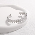 Dettaglio del bracciale argento con motivo a foglie su un vassoio di ceramica bianco - Color Acciaio
