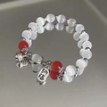 Macro shot of beaded bracelet with white cat-eye stones, silver bell, and lucky charm - Red-Fortune