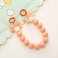 Close-up of orange and cream beaded phone charm with two pink bows on a green tray - Orange