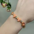 Detail of gold chain bracelet with coral enamel hearts and sparkling zircon stones on wrist - Orange