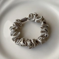 Detailed close-up of a champagne silk scrunchie with a grey matte tube on ceramic - Silver