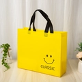 Yellow non-woven tote bag with classic smiley face and black handles on a wooden table - Classic Smiley