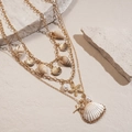 Close-up of golden multi-layer necklace featuring shell, conch, starfish and pearl charms - Three-Piece Set / Gold