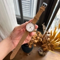 Quartz wristwatch with white dial and brown suede strap held against a natural background - Brown