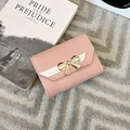 Detailed view of pink tri-fold faux leather wallet with a golden metal bow decoration - Pink