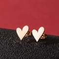 Vue macro de boucles d'oreilles cœur dorées sur support noir et fond rouge vif - Or rose
