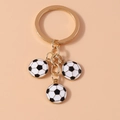 Detail of metal keychain featuring three black and white soccer charms on golden rings - Black