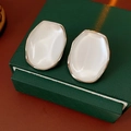 Makroaufnahme minimalistischer weißer ovaler Harzohrringe mit elegantem Goldrand auf Box - Silberstift - Ohrstecker / Silber-Weiß