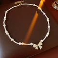 Detalle de collar de perlas con colgante de lazo dorado y circonitas sobre cuero - Dorado con perla blanca
