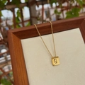 Dettaglio macro di una collana in acciaio al titanio dorato con pendente a lettera G - Lettera G
