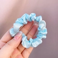 Hand holding a light blue satin scrunchie with smooth texture and pleated design - Light Blue