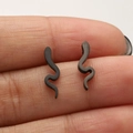 Detailed close-up of matte black snake-shaped punk earrings held between fingers - 674 Snake / Black