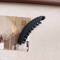 Vista dettagliata di un grande fermaglio a banana nero opaco su una cartolina minimal - Nero