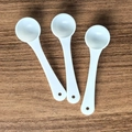 Three white plastic measuring spoons for milk powder placed on a wooden table surface - 1g Short Handle with Hole (8.2*2.2cm) / White