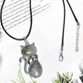 Silver cat pendant with green stone on black wax cord necklace over an open book - Labradorite