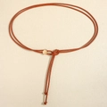 Dettaglio di una sottile corda in pelle marrone con fibbia rotonda dorata e nodi finali - Cammello