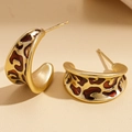 Macro view of C-shaped gold metal earrings with leopard print enamel texture - Gold