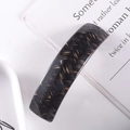 Close-up of a dark brown acetate hair clip with herringbone pattern on a book and plate - 30# Spring Clip (Dark Brown Herringbone)