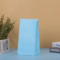 Detail view of a sky blue kraft paper gift bag with serrated edges on a blue desk - Light Blue