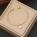 Detail view of a gold open bangle featuring a pink enamel evil eye charm in a jewelry box - Pink