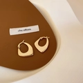 Close-up of elegant gold irregular geometric hoop earrings on a brown leather surface - Irregular Geometric Hoop / Gold